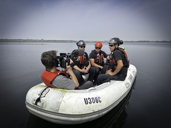 Three firefighters and a cameraman in a boat on a lake.