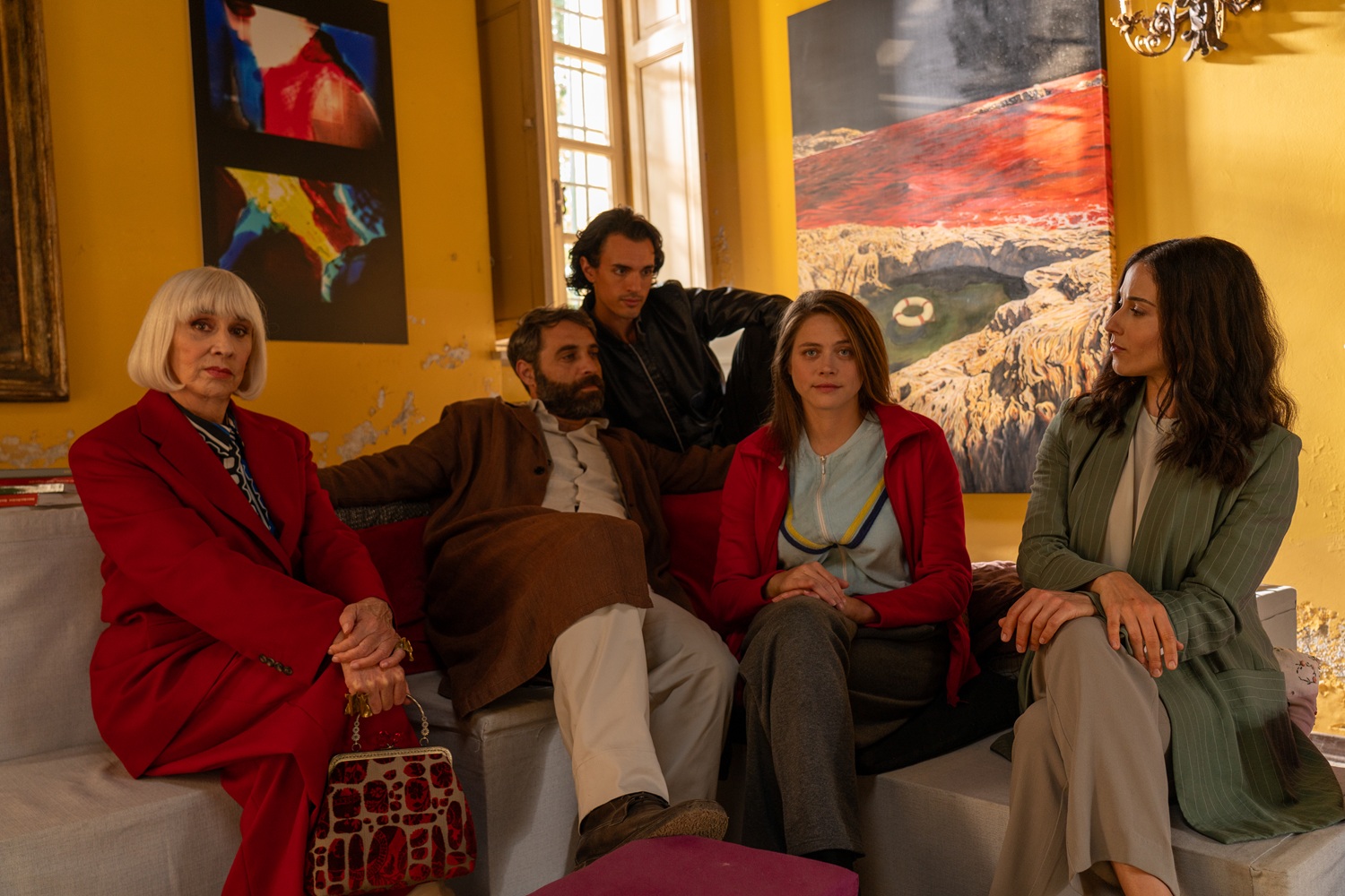 An italian family sit on a white couch in a yellow room with brightly coloured artwork on the walls.