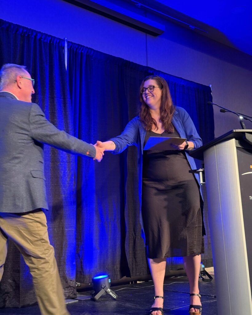 A woman presents an award to a man on stage behind the podium. They wear formal clothes.