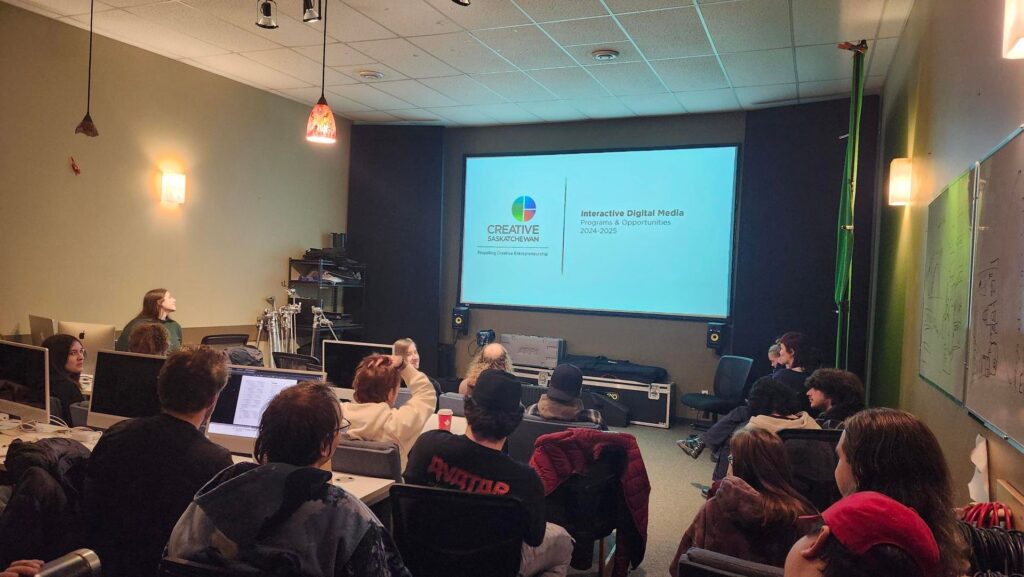 A woman presents on Creative Saskatchewan's Interactive Digital grants to a room of young students.