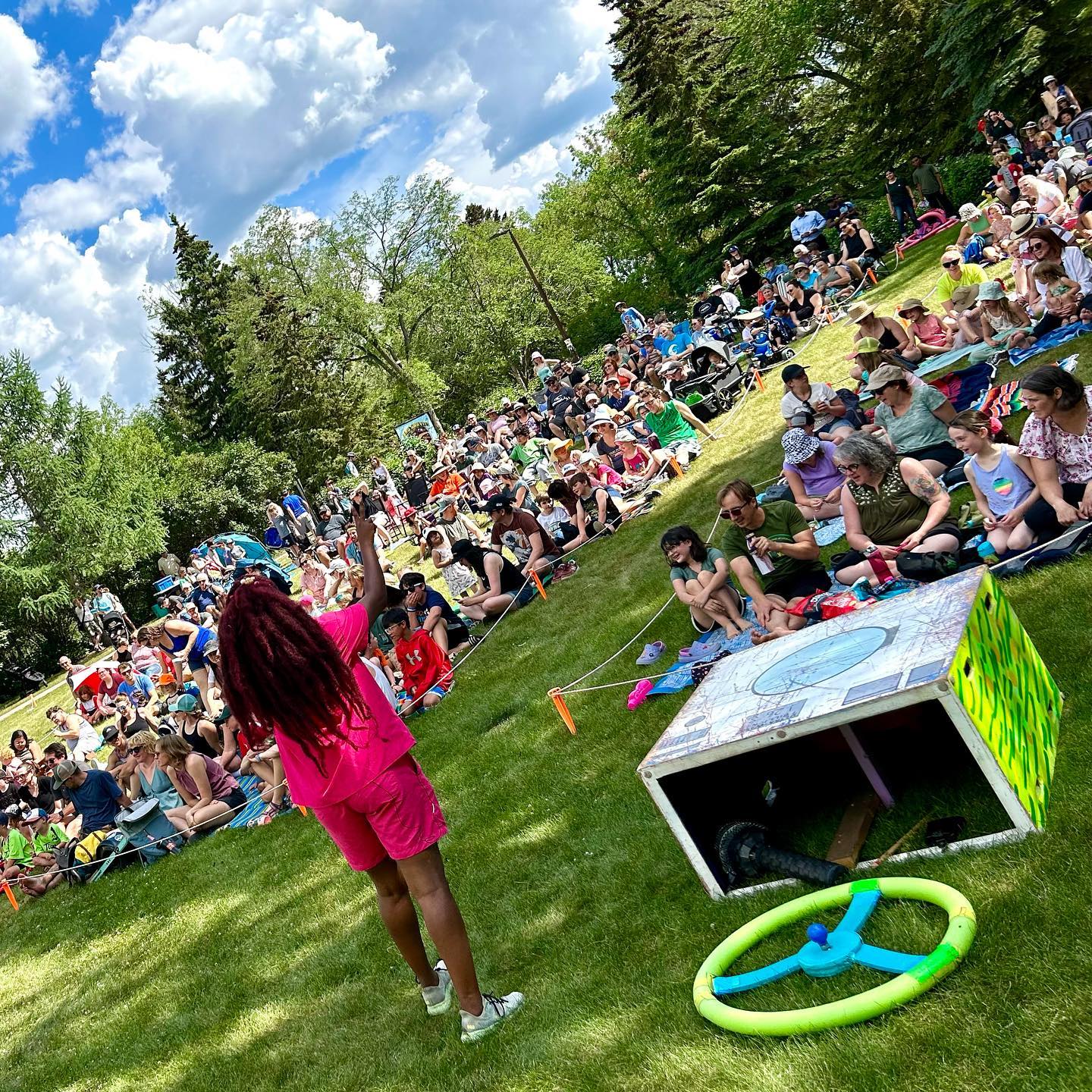 A black woman wearing a pink suit performs in front of a large crowd of families in a park.